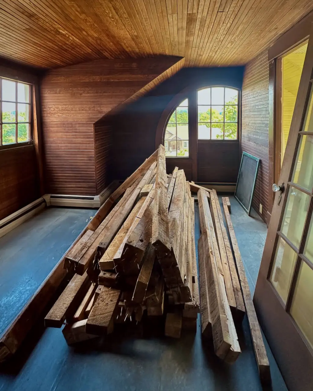 An unfinished wood-paneled interior with lumber stacked on the floor